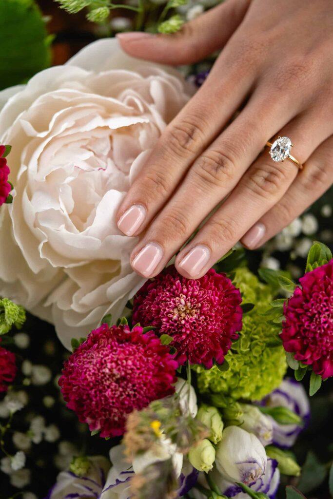 Close-up of engagement ring on bride’s hand resting on a bouquet of pink and white flowers