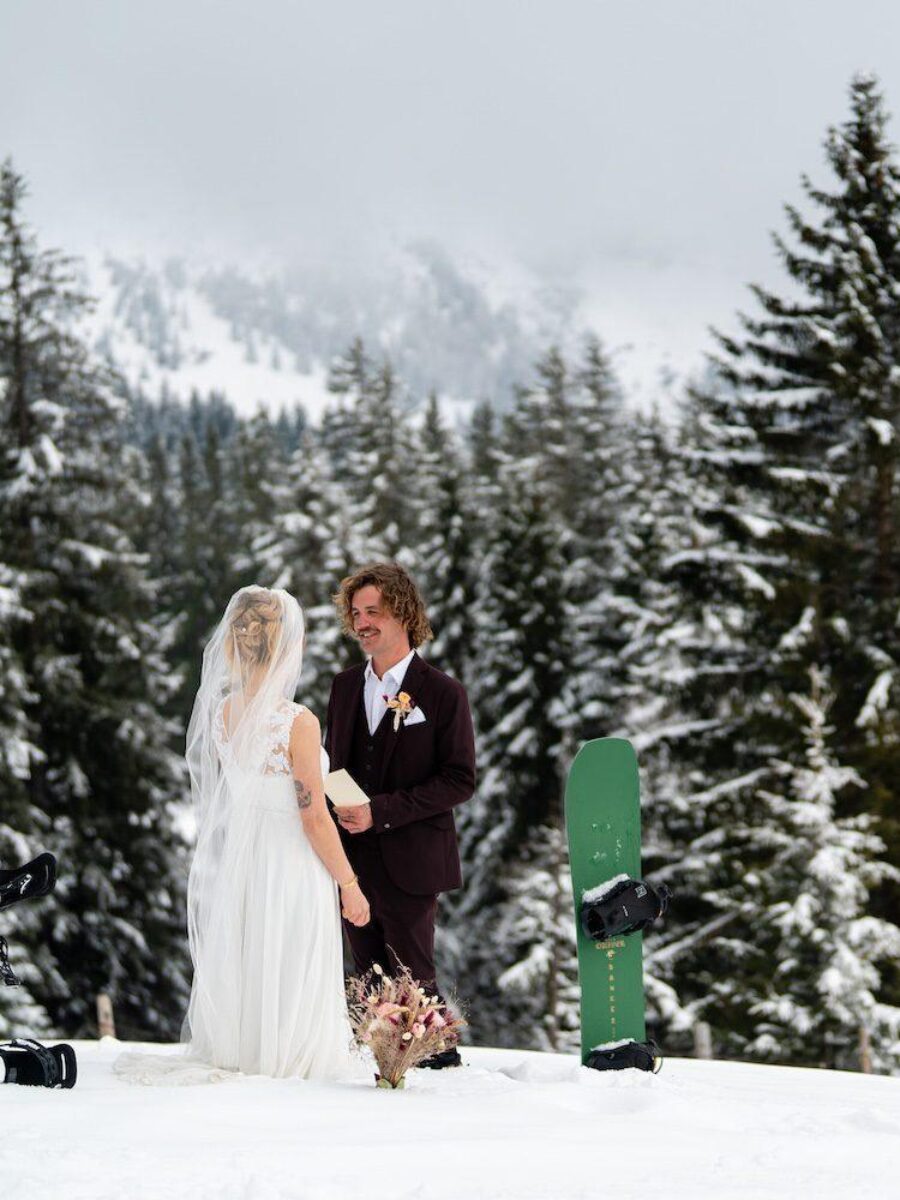 Bride and groom exchanging vows in snowy forest during a winter ski elopement in Grindelwald, Switzerland — snowboards in the foreground.