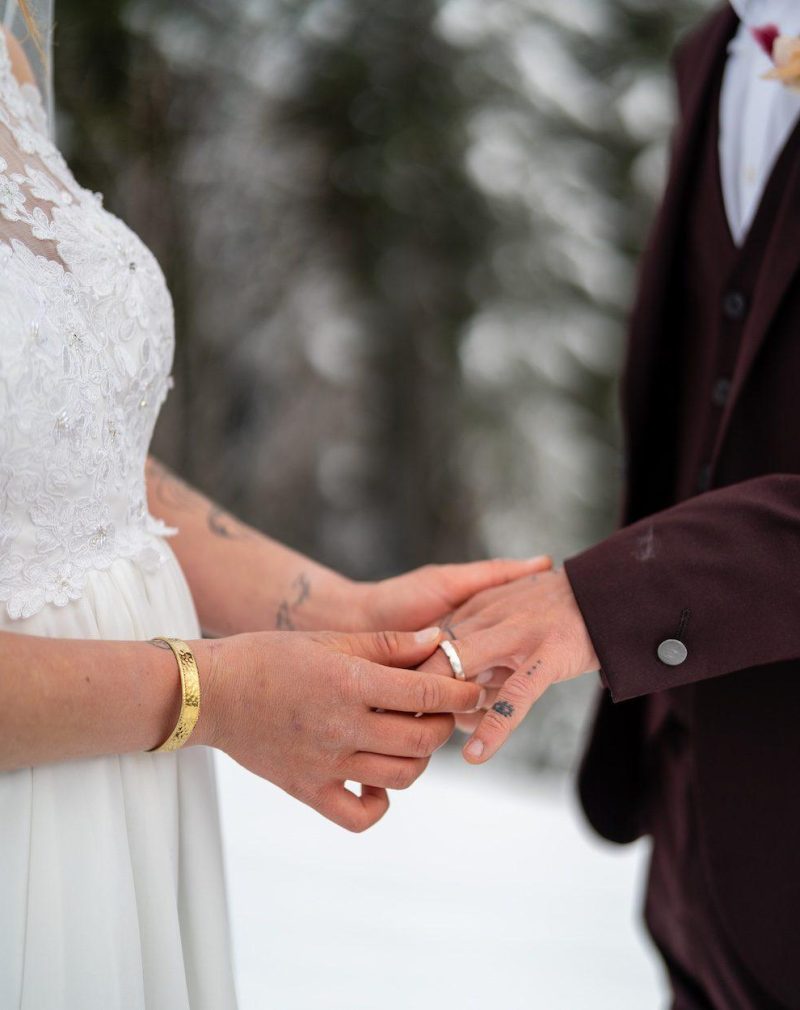 Winter Ski Elopement Wedding Grindelwald First Switzerland Bride and groom exchanging ring in snowy forest during a winter ski elopement in Grindelwald, Switzerland — snowboards in the foreground.