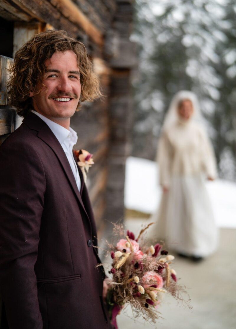 Bride and groom in snowy forest during a winter ski elopement in Grindelwald, Switzerland — snowboards in the foreground.